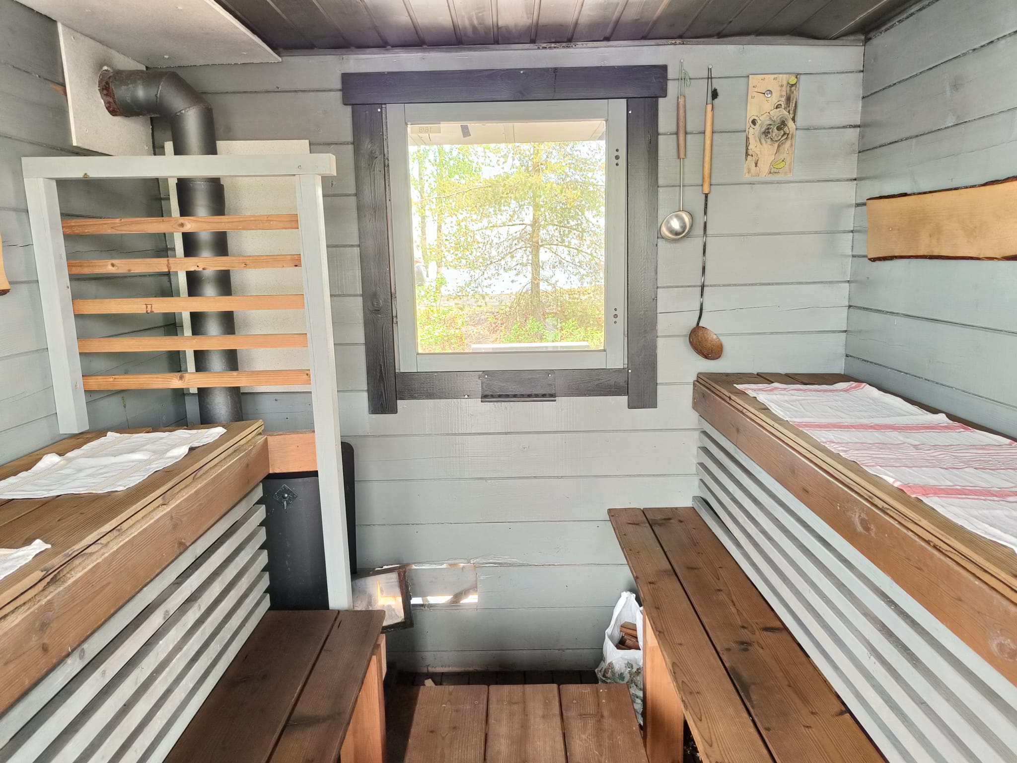 Puulämmitteinen sauna saunalautalla, lauteet ja ikkuna järvelle